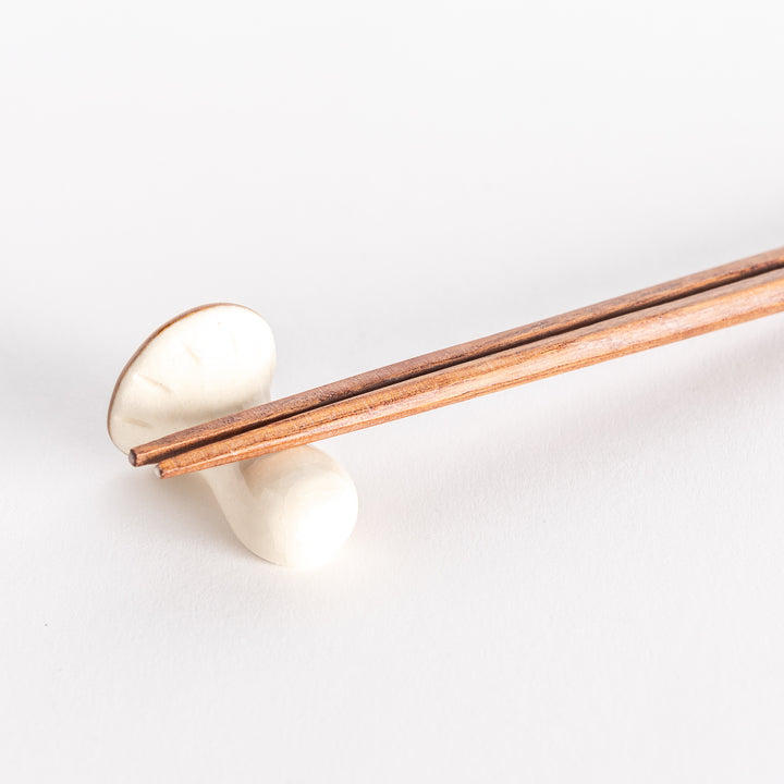 A close-up of a porcini mushroom chopsticks rest with chopsticks resting across its stem.