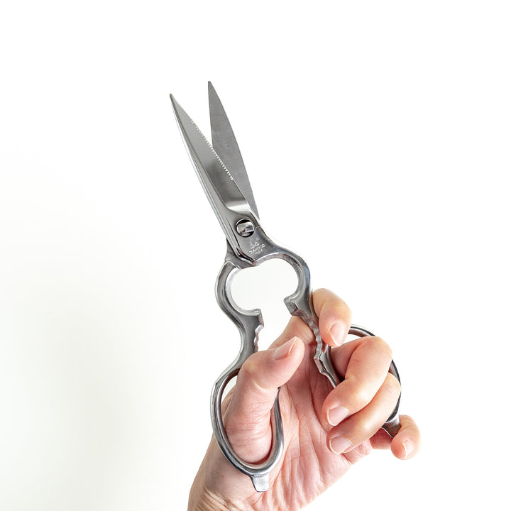 Kitchen shears held firmly in hand, showcasing ergonomic handle and sharp blades for precision cutting in culinary tasks.