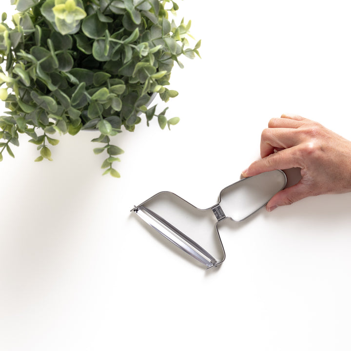 Hand holding a stainless steel peeler with a sharp blade and ergonomic handle, a durable kitchenware tool for easily peeling fruits and vegetables.