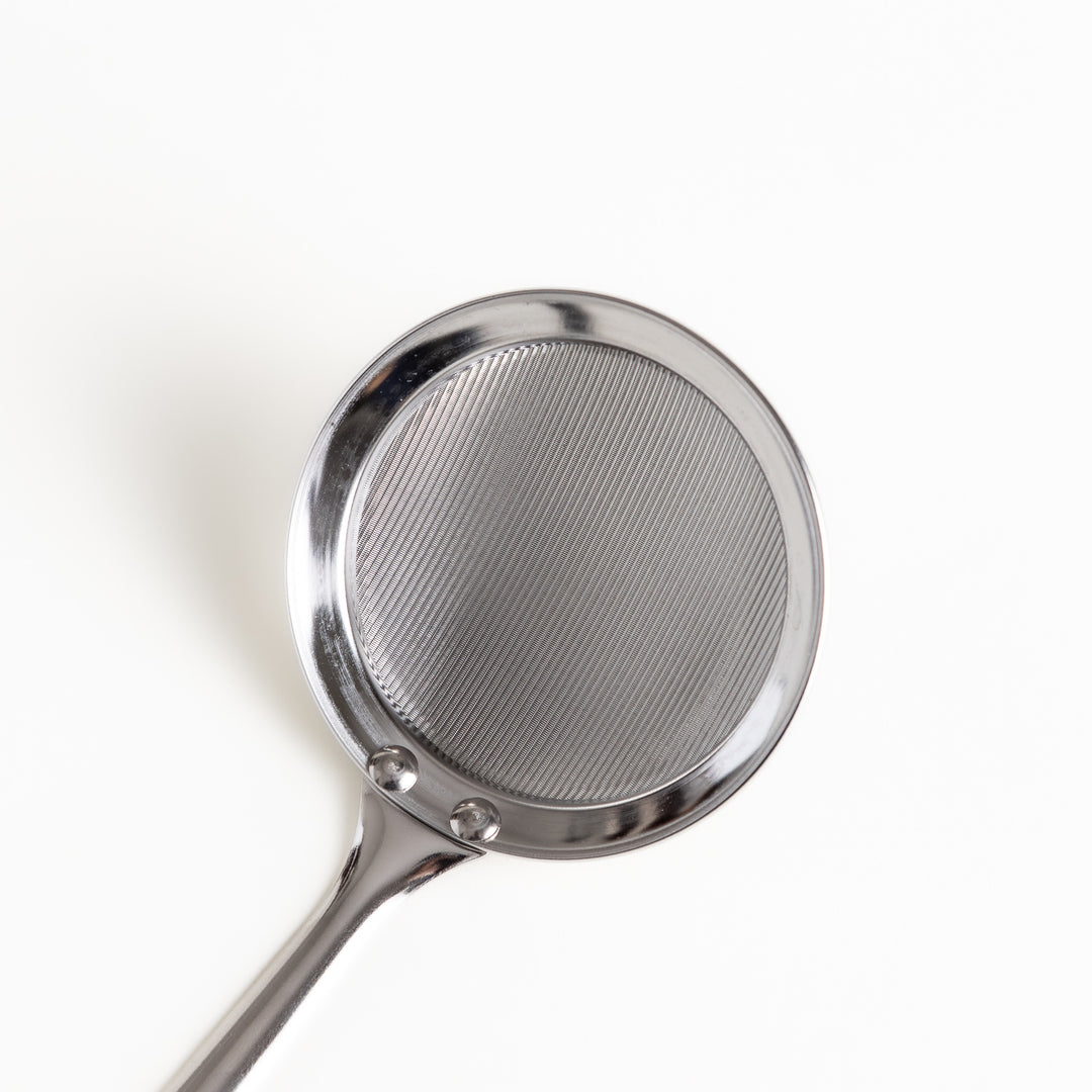 Stainless steel skimmer with a fine mesh net and a long handle, an essential kitchenware tool for removing scum and impurities from broths and soups.