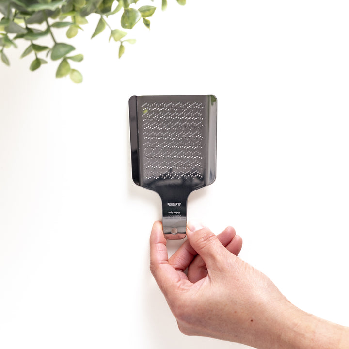 Hand holding a stainless steel wasabi grater with a fine textured surface, an essential kitchenware tool for grating fresh wasabi.