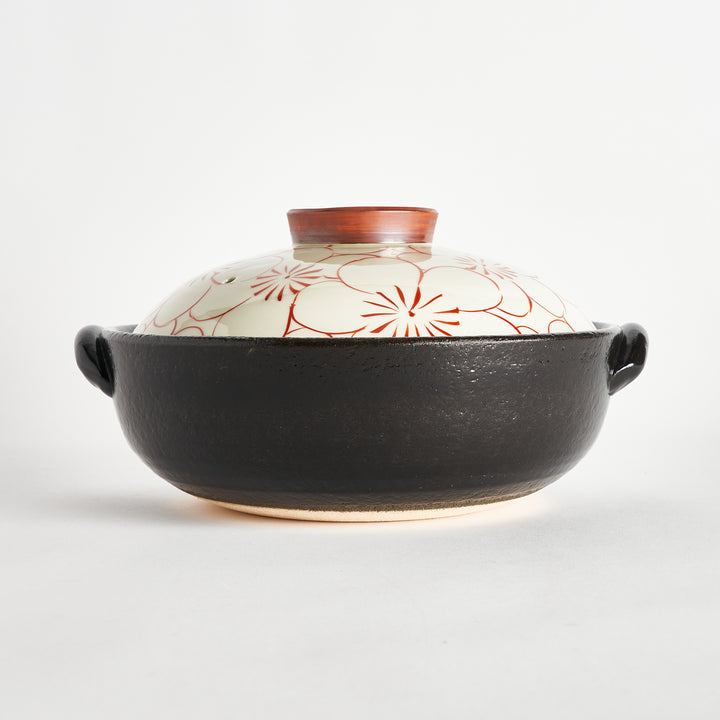 Side view of the donabe showing the black base and the lid decorated with red floral patterns, with a small ceramic top.