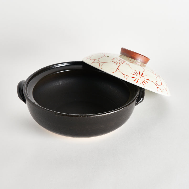 The donabe with the lid slightly lifted, revealing the black inner pot and the white floral lid with red outlines.