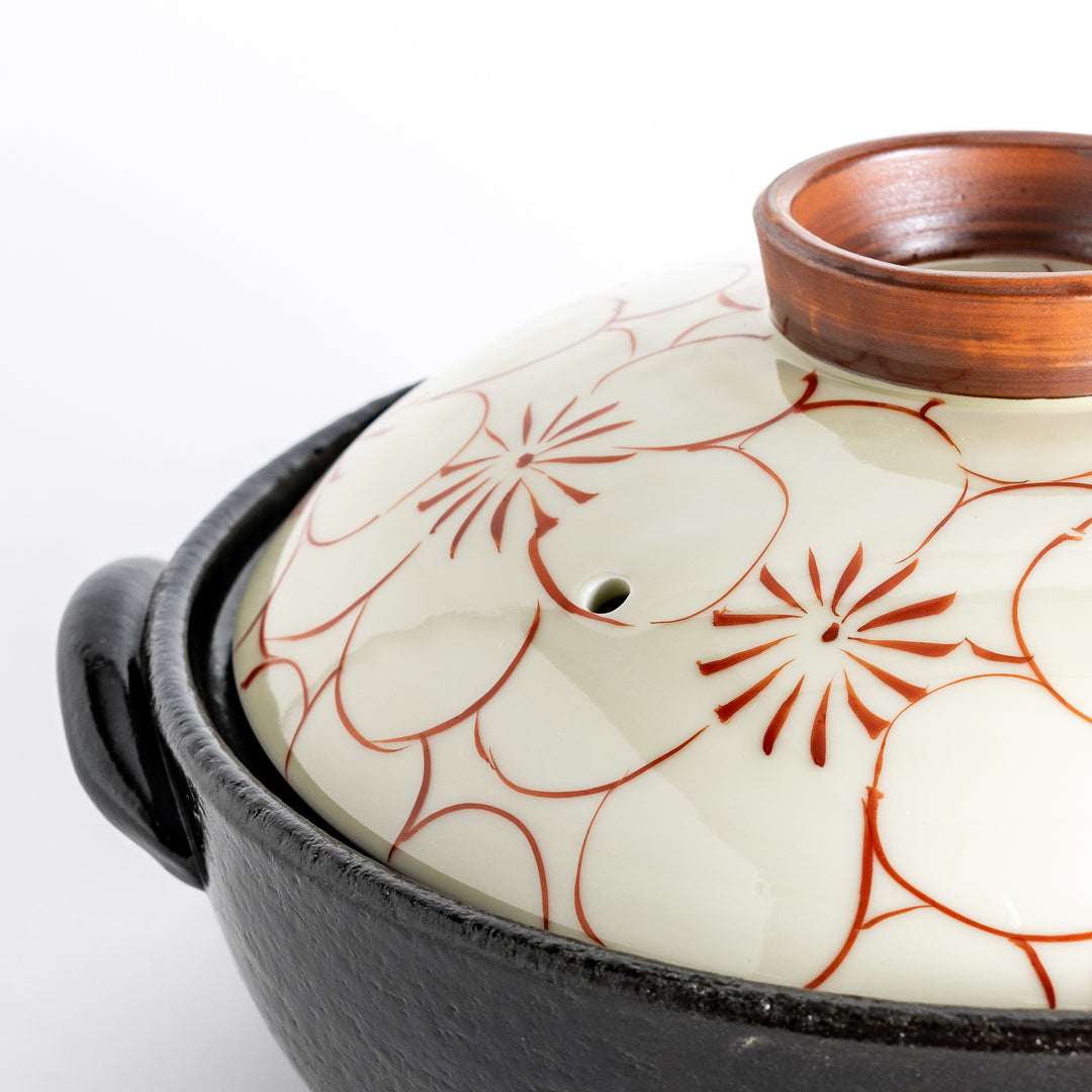 A donabe with a vibrant red floral pattern on white lid and black pot.