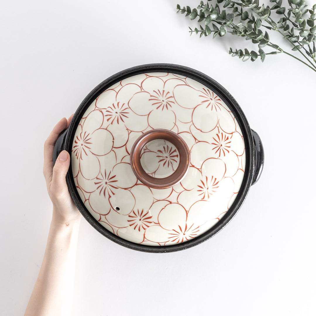 A donabe with a vibrant red floral pattern on white lid and black pot.