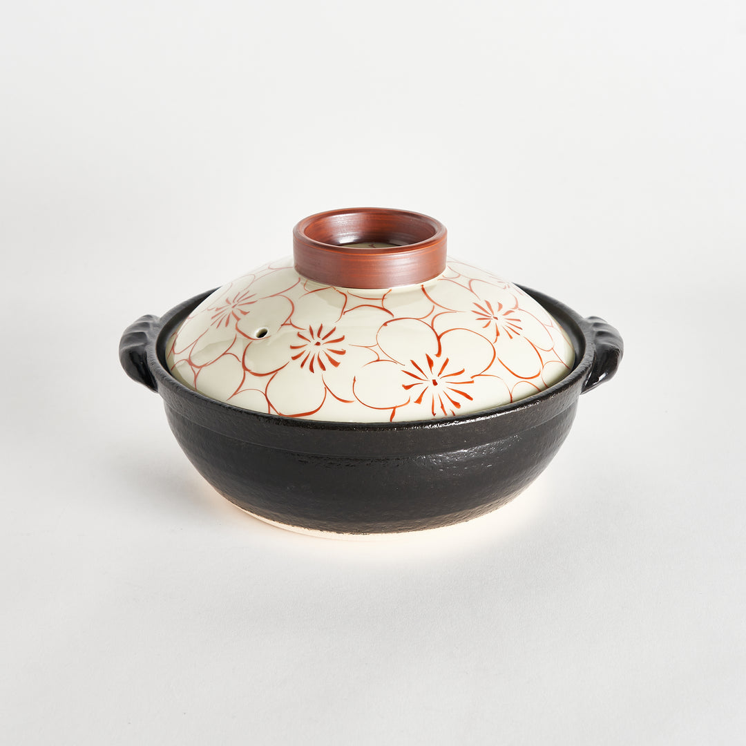 Black donabe with a red blossom-patterned lid featuring a brown ring around the lid’s top, showing the opening on the top.