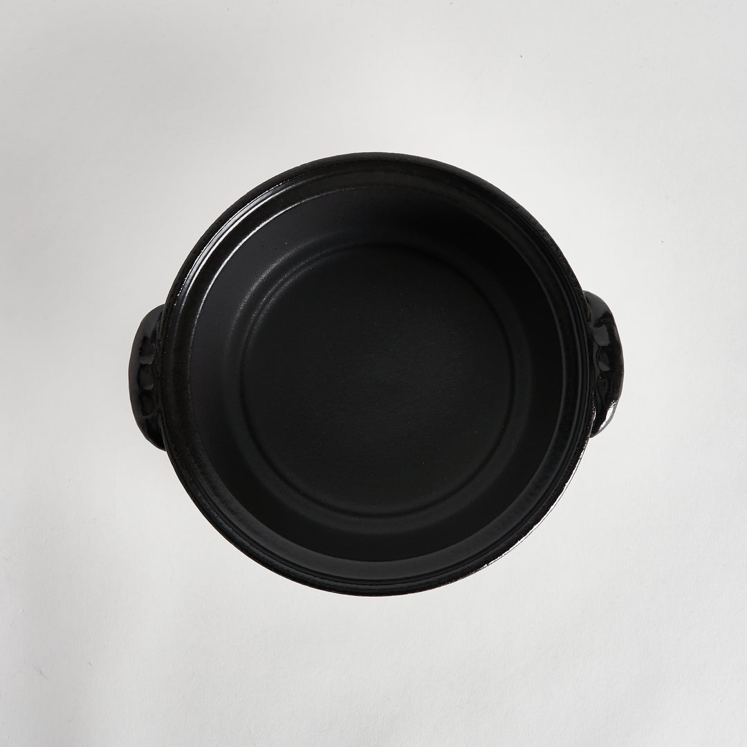 Top-down view of the inside of the black donabe, showing a smooth, black surface and no lid.