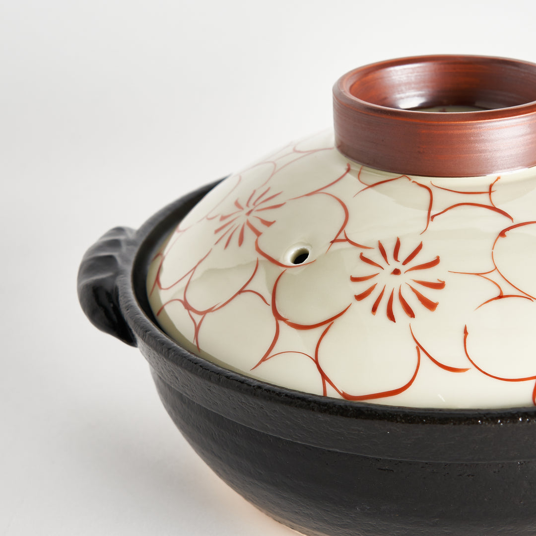 Close-up of the black donabe with a red blossom-patterned lid, focusing on the lid with the brown ring.