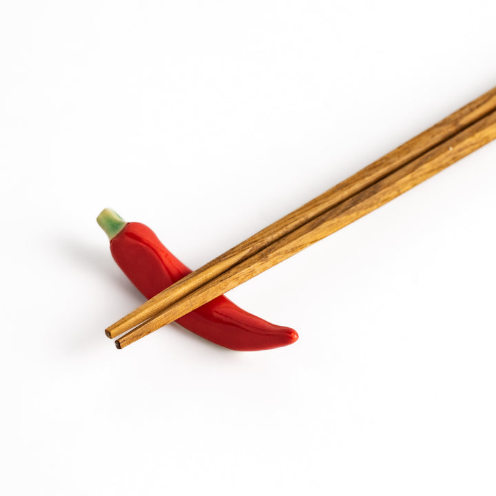 Wooden chopsticks resting on a red chili pepper-shaped chopstick rest, combining practical use and playful design.