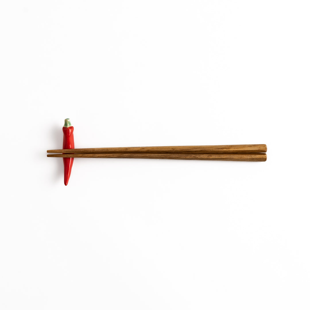 Wooden chopsticks resting on a red chili pepper-shaped chopstick rest, combining practical use and playful design.