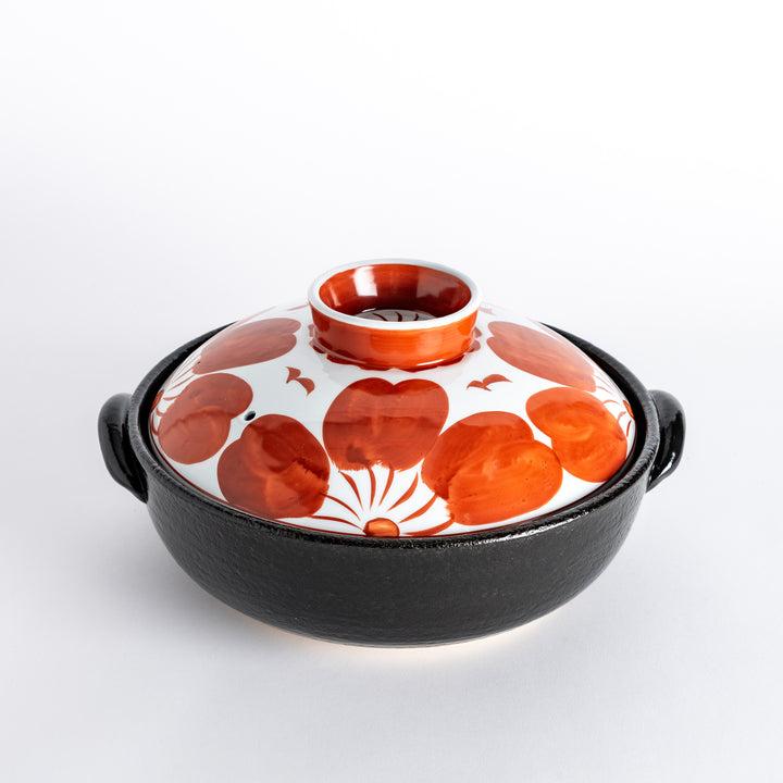 A beautifully crafted donabe with a vibrant red floral pattern on the lid, perfect for serving various hot dishes.