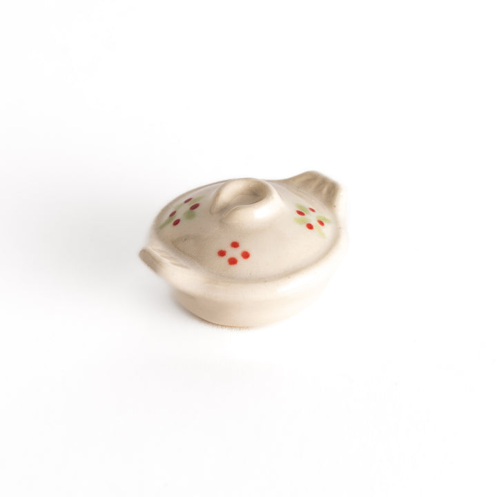 Small earthen pot-shaped chopsticks rest with red flower and green leaf patterns on a beige surface, showcasing a charming, rustic design.