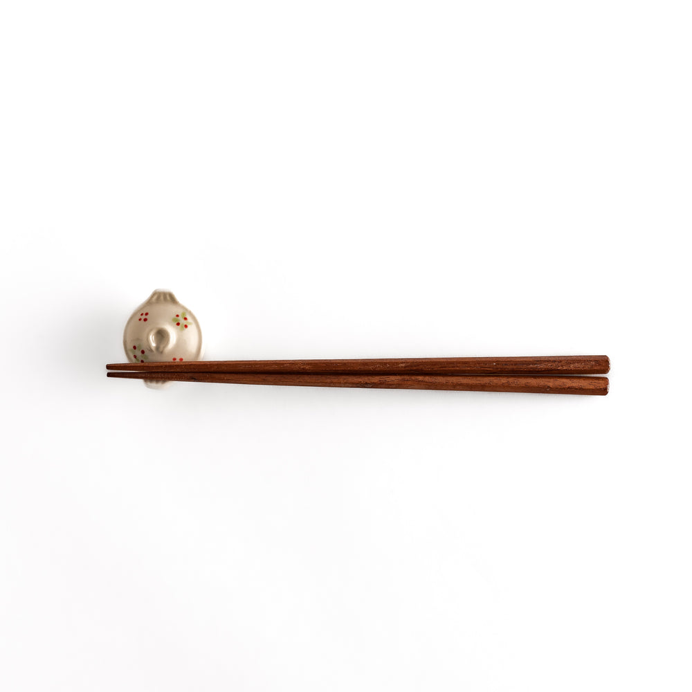 Distant view of chopsticks resting on the earthen pot-shaped chopsticks rest, highlighting its delicate floral patterns and unique shape.