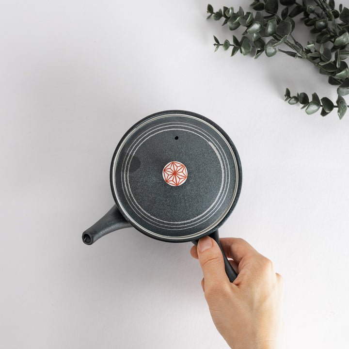 A hand holds the Red Hemp Black Teapot, emphasizing its stylish design and intricate red hemp details against a white backdrop.