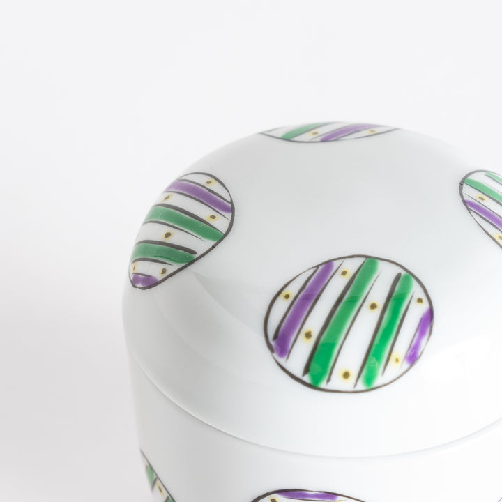 Close-up of the lid of a white bowl showcasing alternating green and purple striped circles.