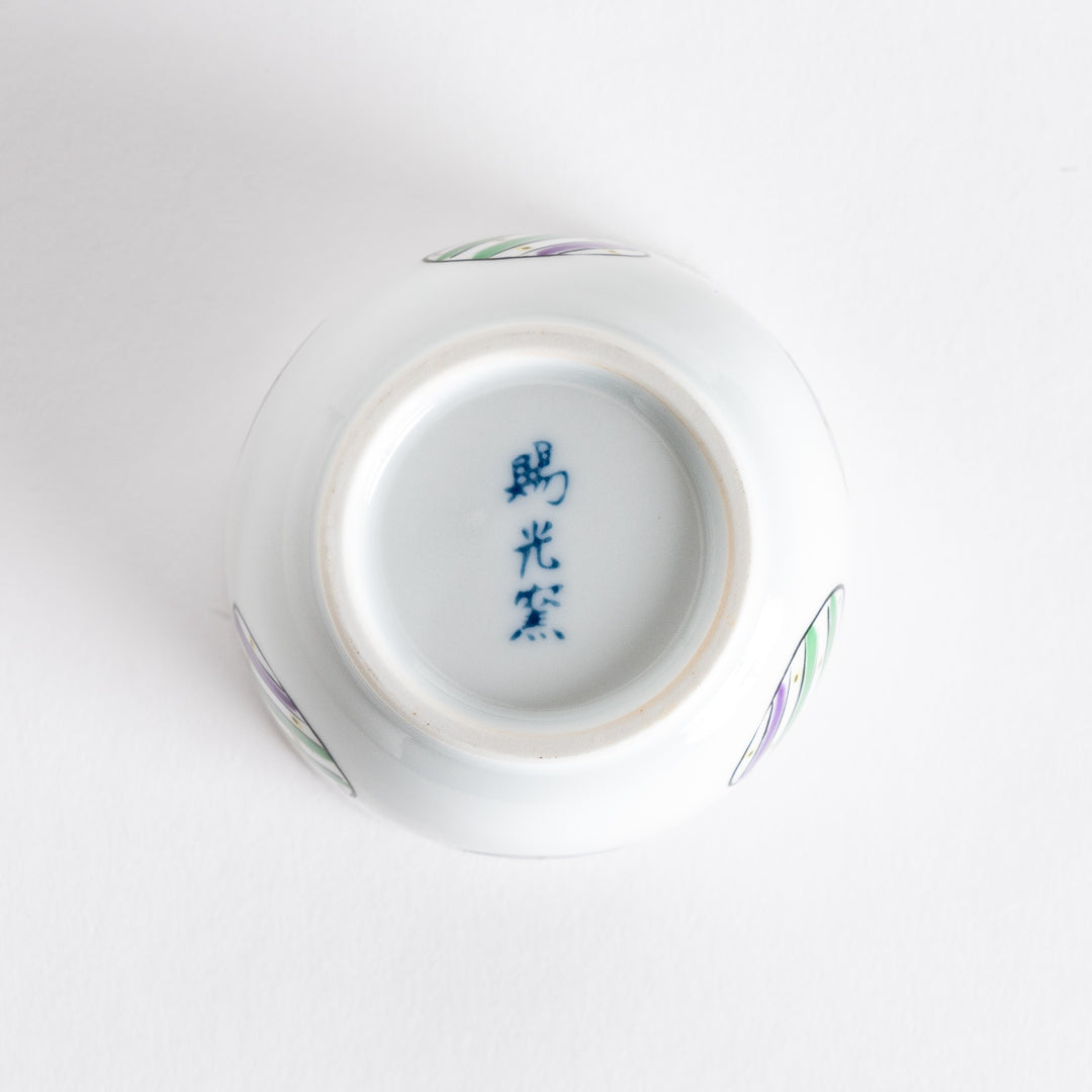 Bottom view of a white bowl featuring alternating green and purple striped circles on the sides.