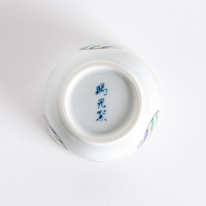 Bottom view of a white bowl featuring alternating green and purple striped circles on the sides.