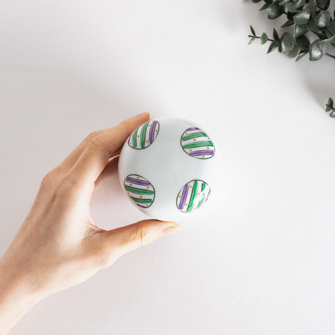 Top view of a white bowl featuring alternating green and purple striped circles on the lid.