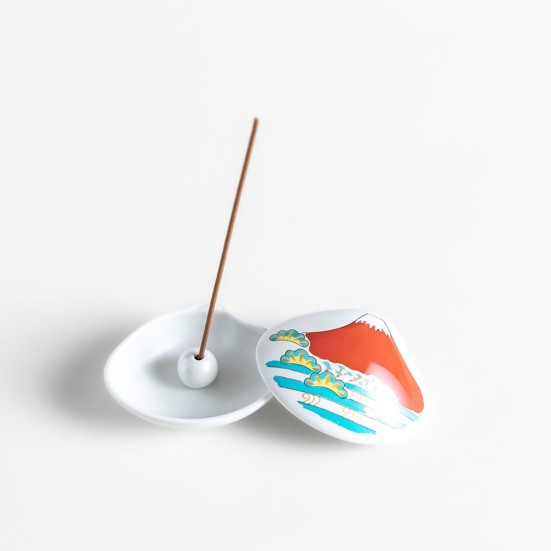 White ceramic incense holder shaped like a seashell, showcasing a striking red Mount Fuji design with golden accents and a secure incense stand inside for refined elegance.