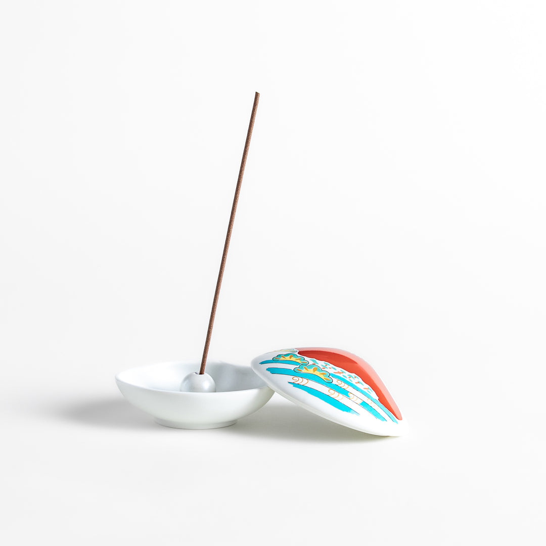 White ceramic incense holder shaped like a seashell, showcasing a striking red Mount Fuji design with golden accents and a secure incense stand inside for refined elegance.