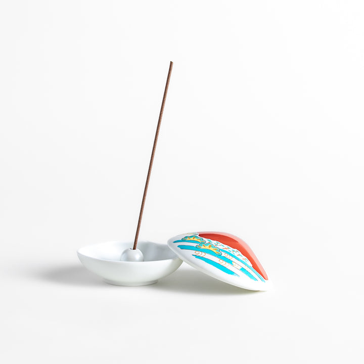 White ceramic incense holder shaped like a seashell, showcasing a striking red Mount Fuji design with golden accents and a secure incense stand inside for refined elegance.