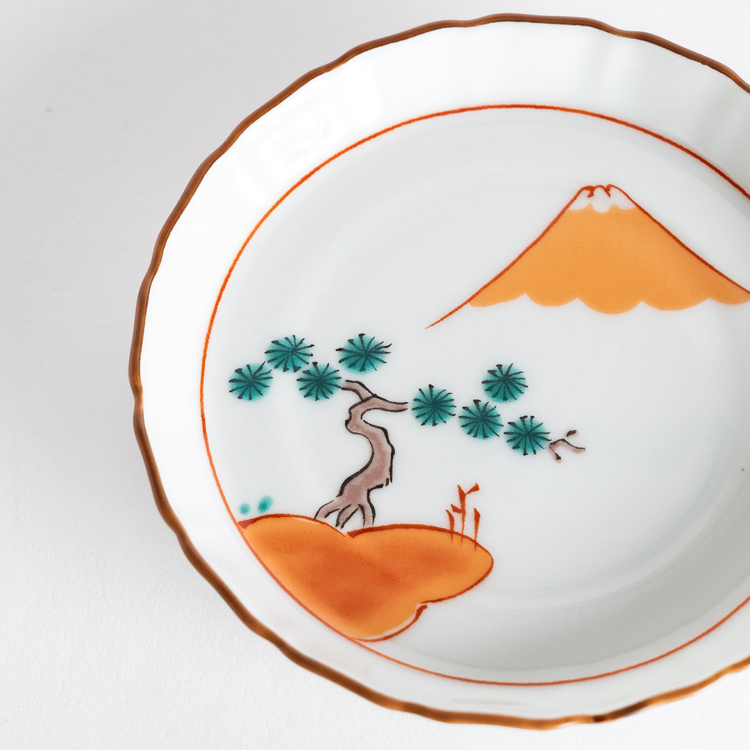 Close-up view of a round dish displaying the intricate design of Mount Fuji and red pine trees, accentuated by a delicate orange rim.