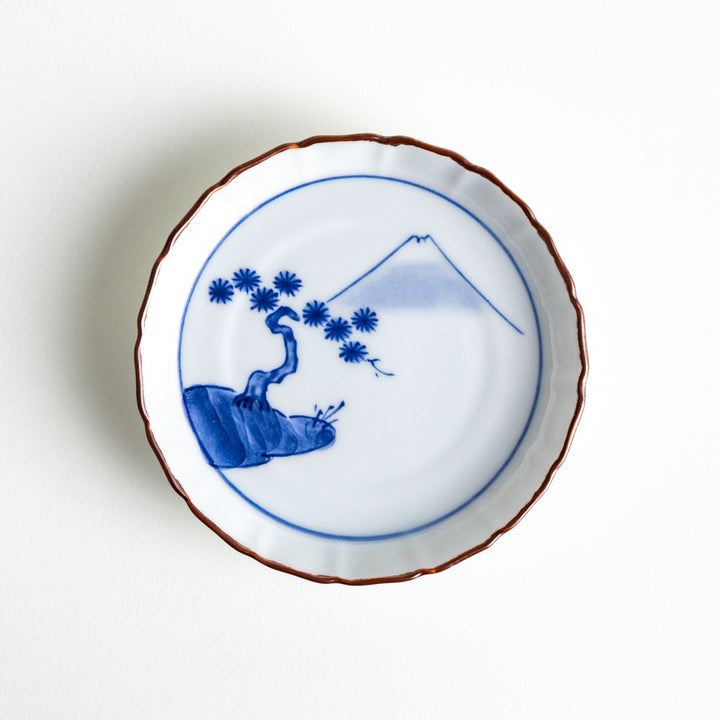 Top view of a porcelain sauce dish with a raised rim, featuring a blue Mount Fuji motif and classical pine tree scene with a brown edge accent.