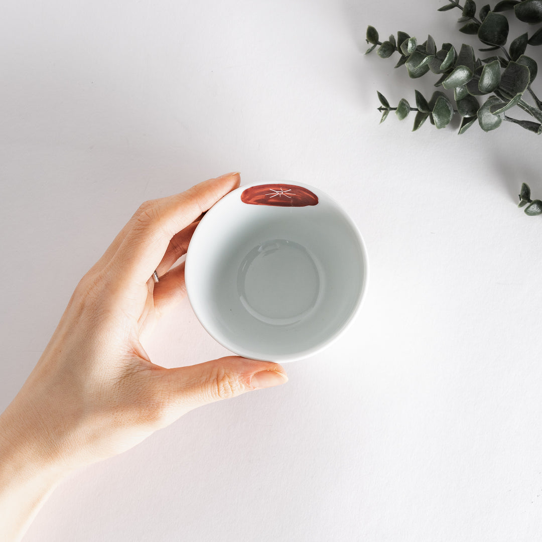 Top view of a white teacup held in hand, displaying its artistic red detailing and smooth interior.