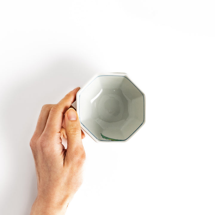 Hand-holding an octagonal white porcelain dessert bowl with colorful turnip and leaf designs, highlighting its unique structure and artistry.