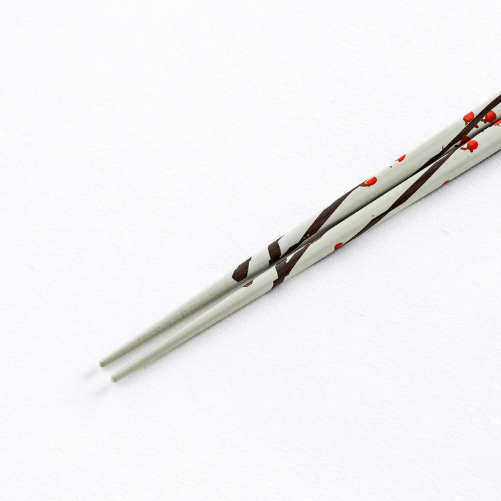 Close-up of the tip of a white chopstick with red plum blossom patterns, highlighting the delicate design.