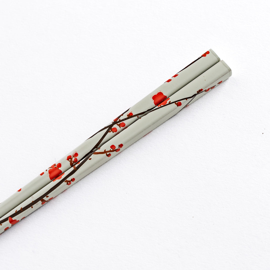 Close-up of the handle of a white chopstick with red plum blossom patterns, displaying the intricate details of the design.