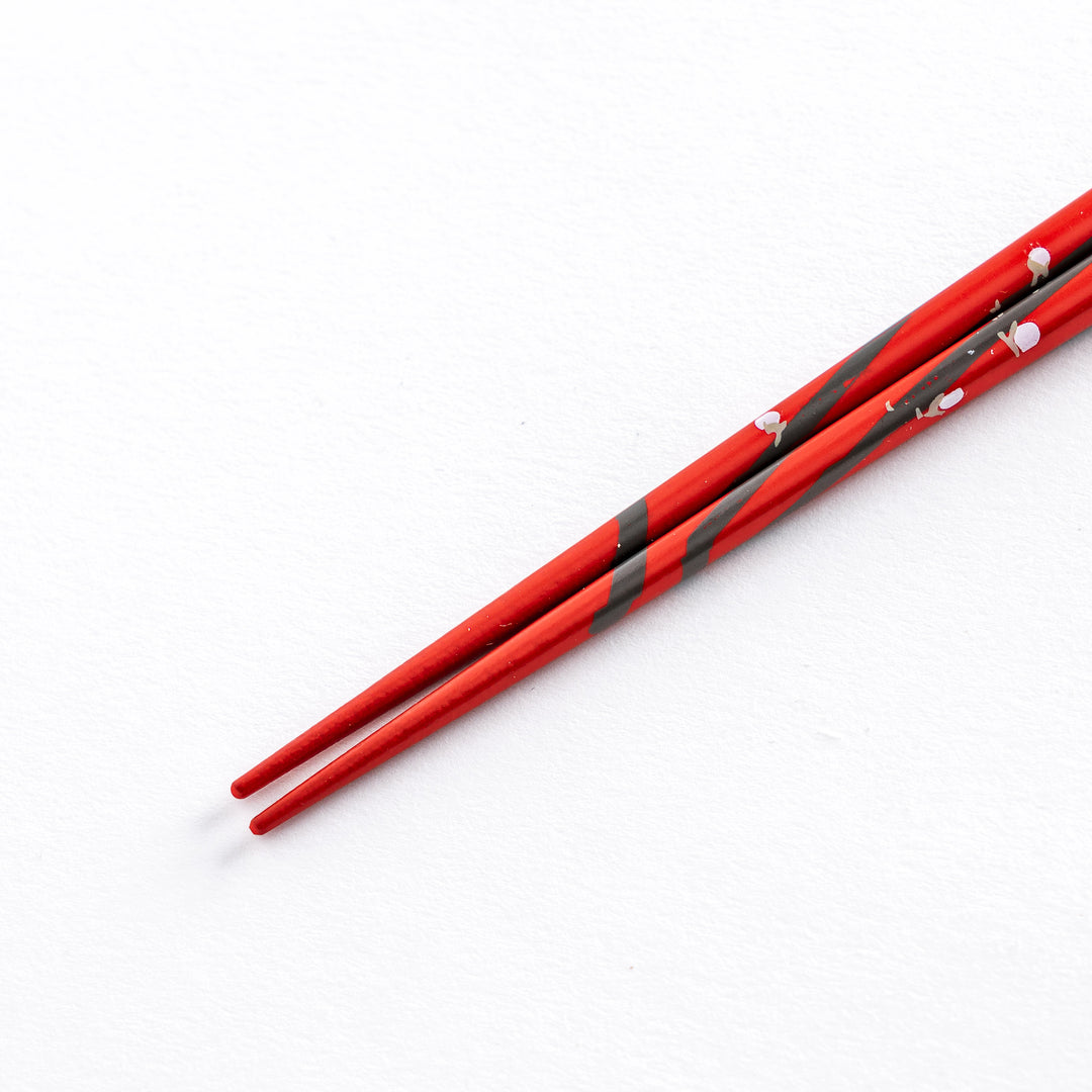 Close-up of the tip of a red chopstick with white plum blossom patterns, highlighting the delicate design.