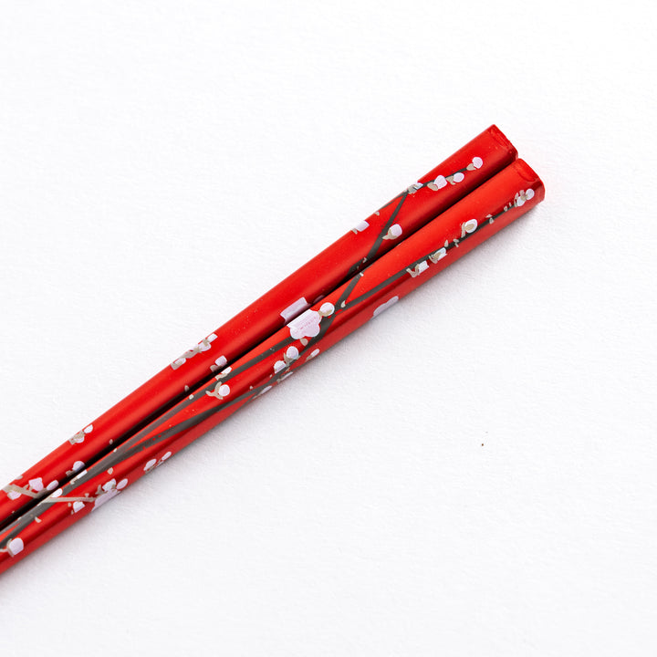 Close-up of the handle of a red chopstick with white plum blossom patterns, displaying the intricate details of the design.