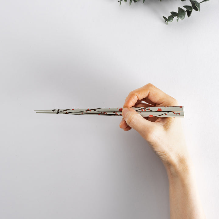 Holding a red chopstick with white plum blossom patterns in hand, highlighting its traditional and refined look.