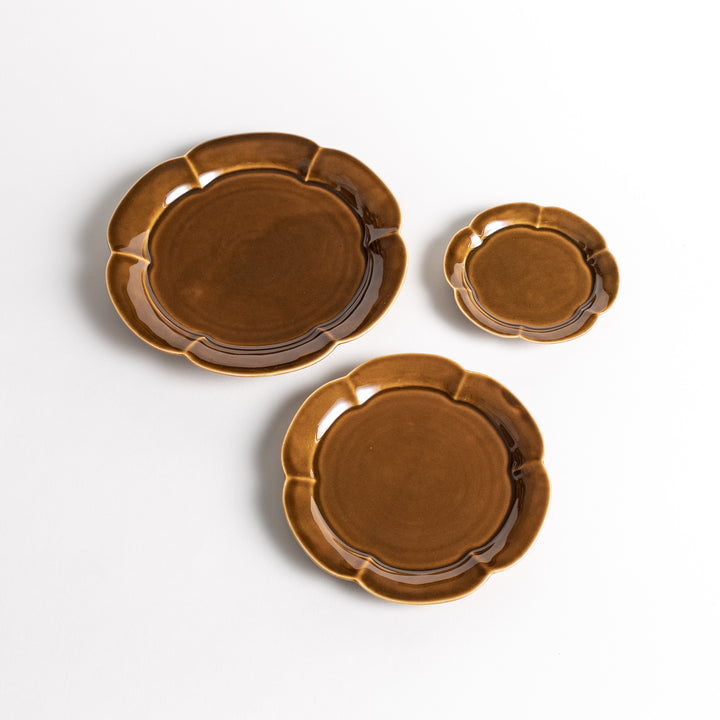 Three brown, flower-shaped ceramic plates of different sizes. The plates have a glossy finish with slightly raised edges and a warm, earthy color.