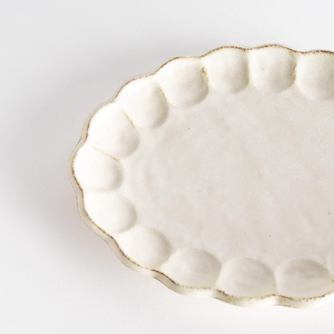 A white ceramic serving plate with a delicate, scalloped oval shape. Available in black or white.