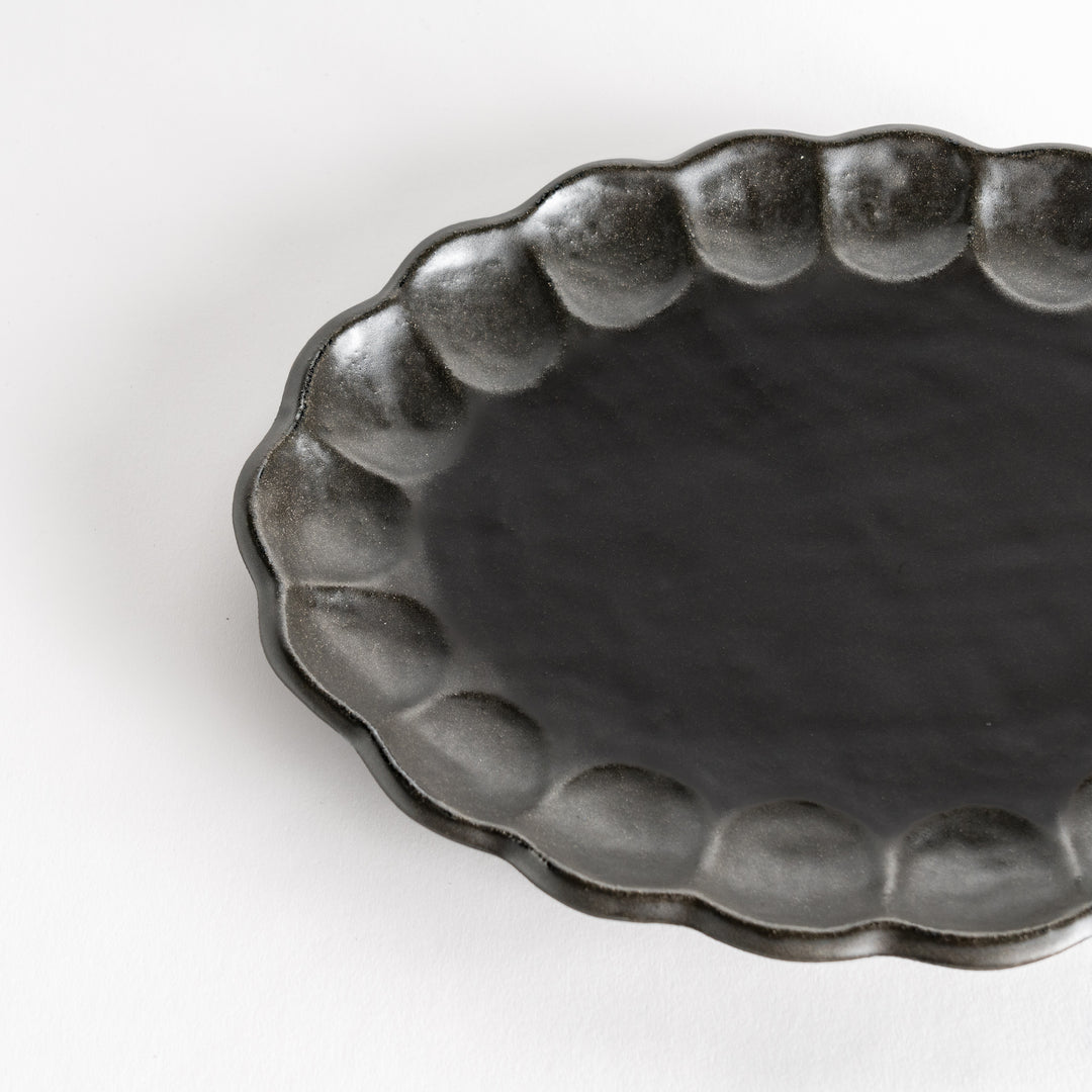 A white ceramic serving plate with a delicate, scalloped oval shape. Available in black or white.