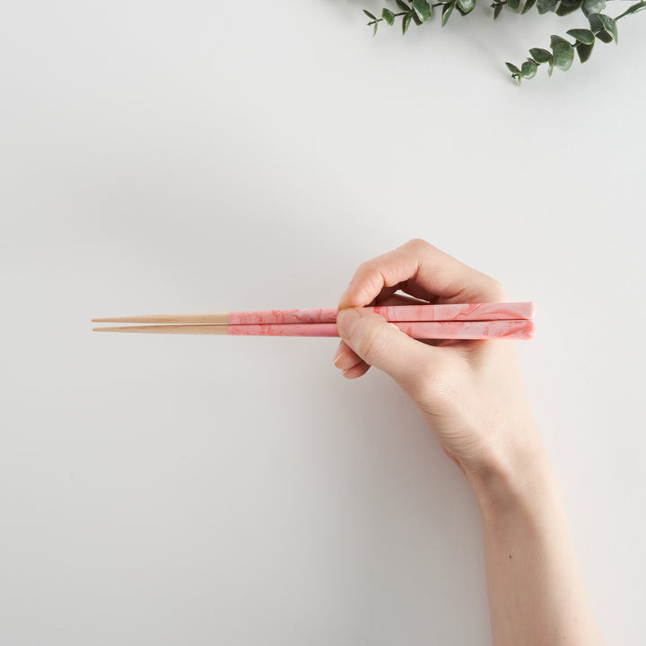 Rose Petal Fusion Chopsticks in hand, showcasing their delicate pink marbled design. The elegant look is complemented by the natural wood color of the handles.