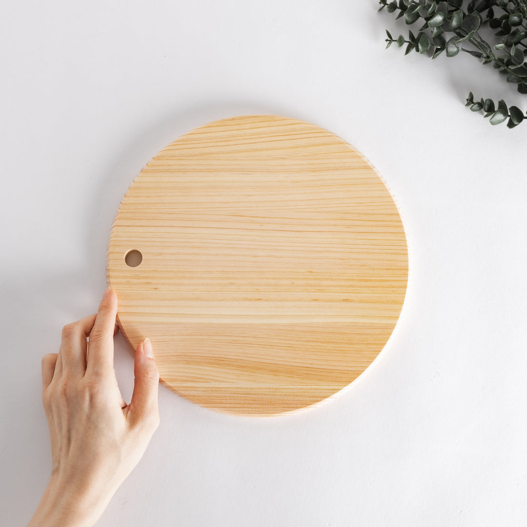 Person holding a round Hinoki cutting board with a hole.