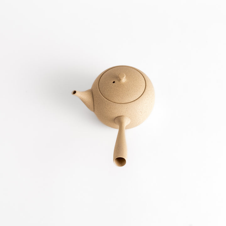 Angled view of the teapot highlighting its textured beige surface and smooth, rounded form.