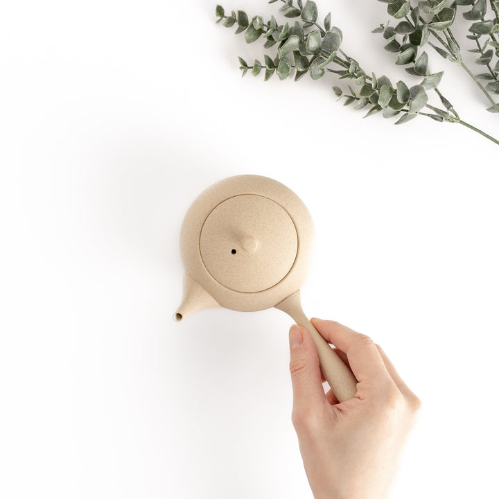 Top-down view of the teapot with a hand gently holding the side handle, emphasizing its ergonomic design.