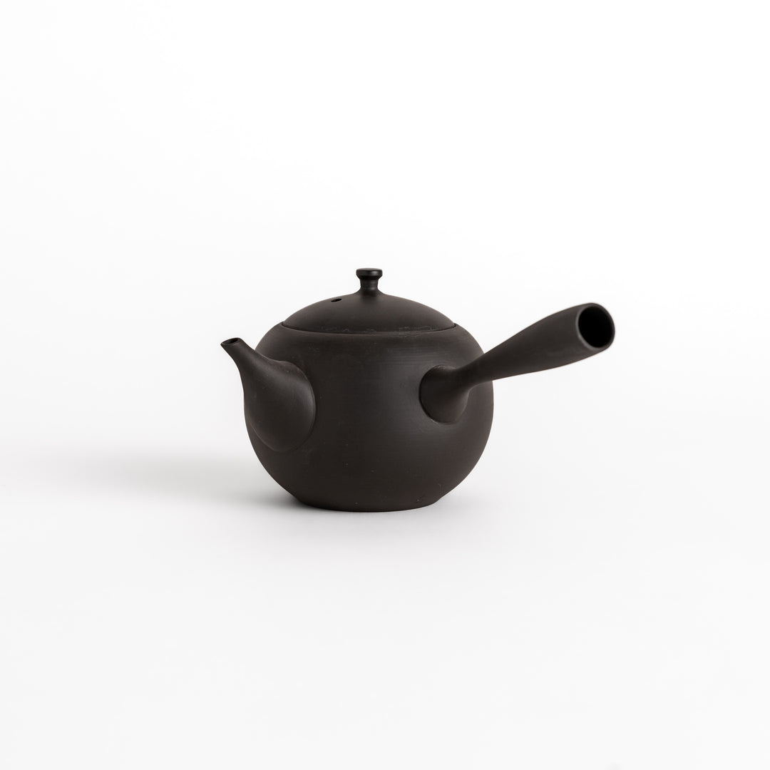 Minimalist black ceramic teapot with a round shape and side handle, showcasing its elegant and functional design.