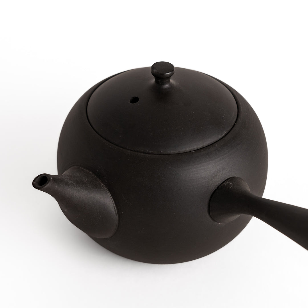 Close-up of the black teapot, showcasing the texture and craftsmanship of the ceramic material.