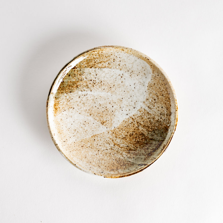 A small dessert plate with a speckled cream and brown glaze, featuring an organic, earthy design.