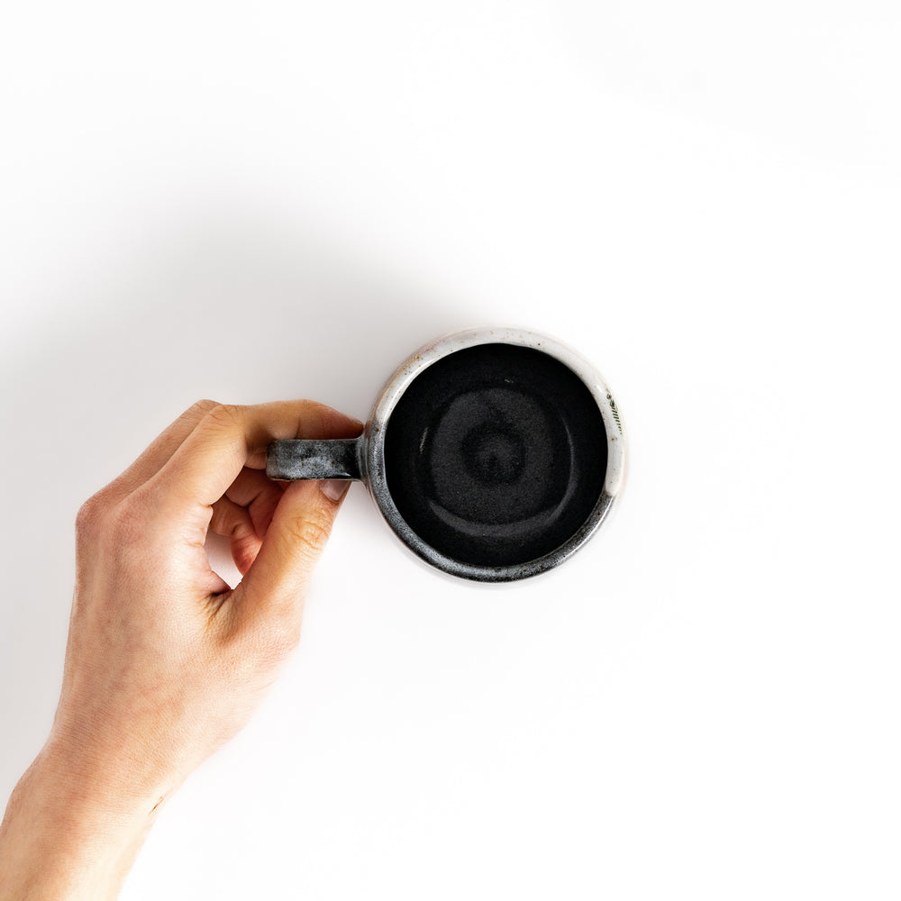 Hand holding a mug with a unique speckled glaze, viewed from above.