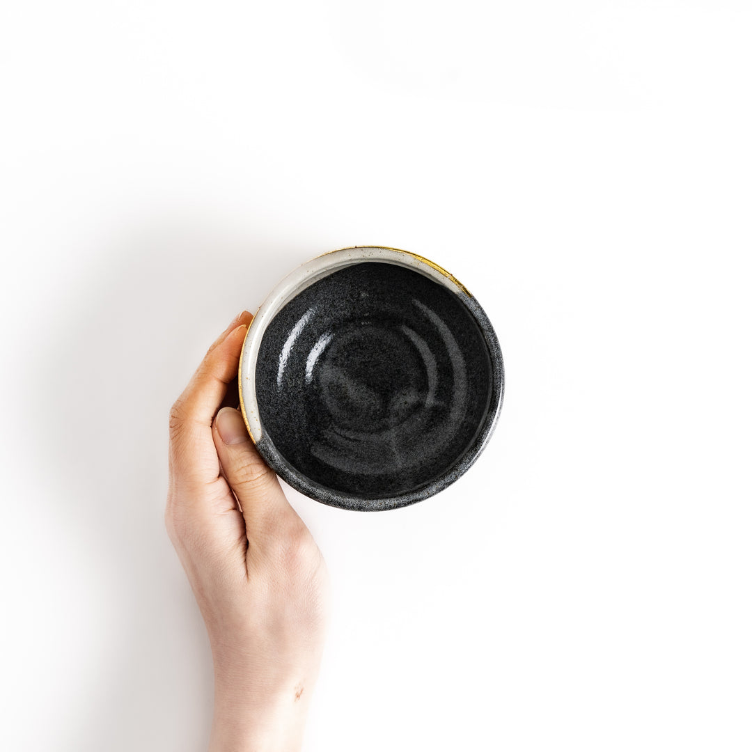 Hand holding a black matcha bowl with a gold accent and a unique glaze, perfect for whisking and savoring a delicious cup of matcha.