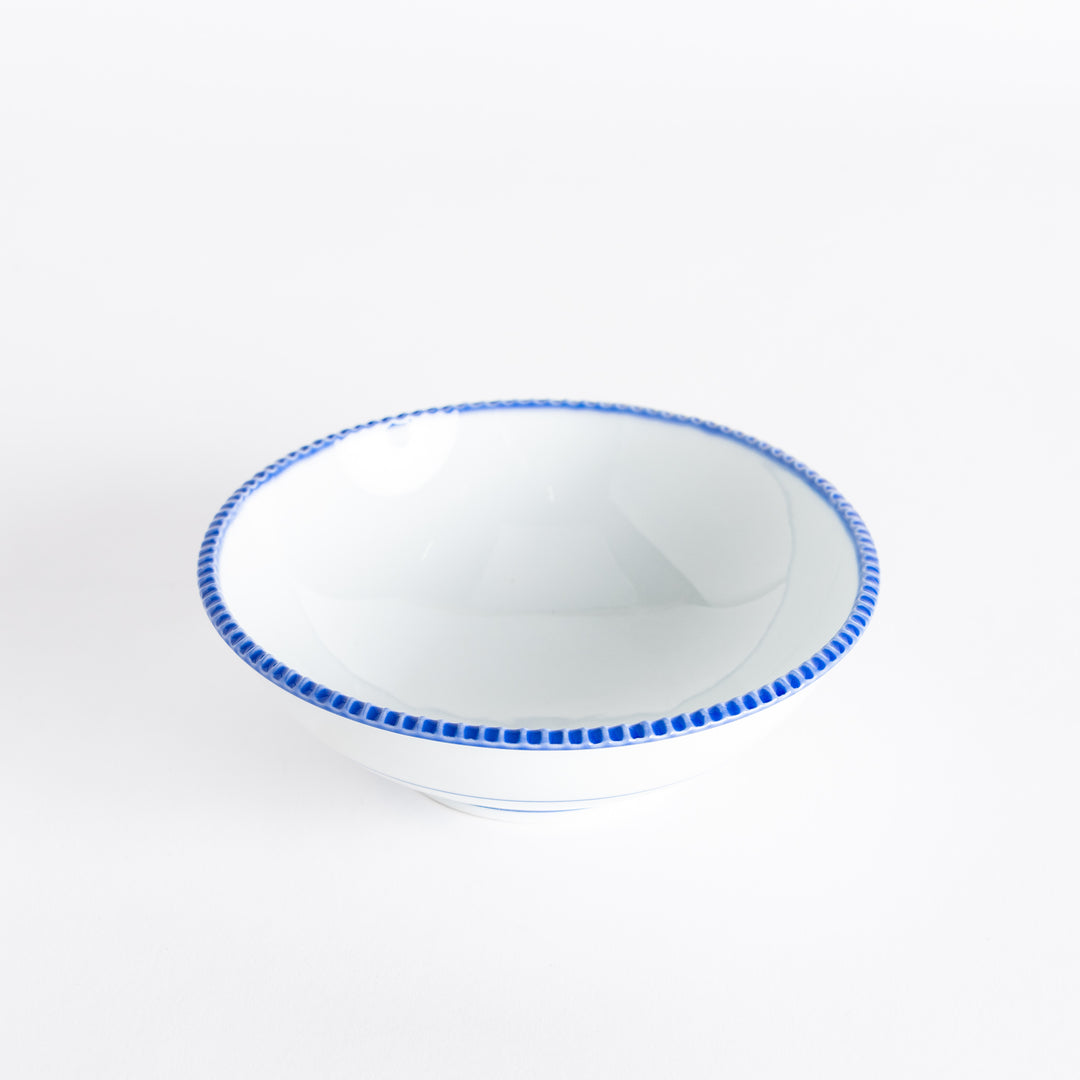 Top view of a cereal bowl featuring a smooth white interior and a blue scalloped edge.