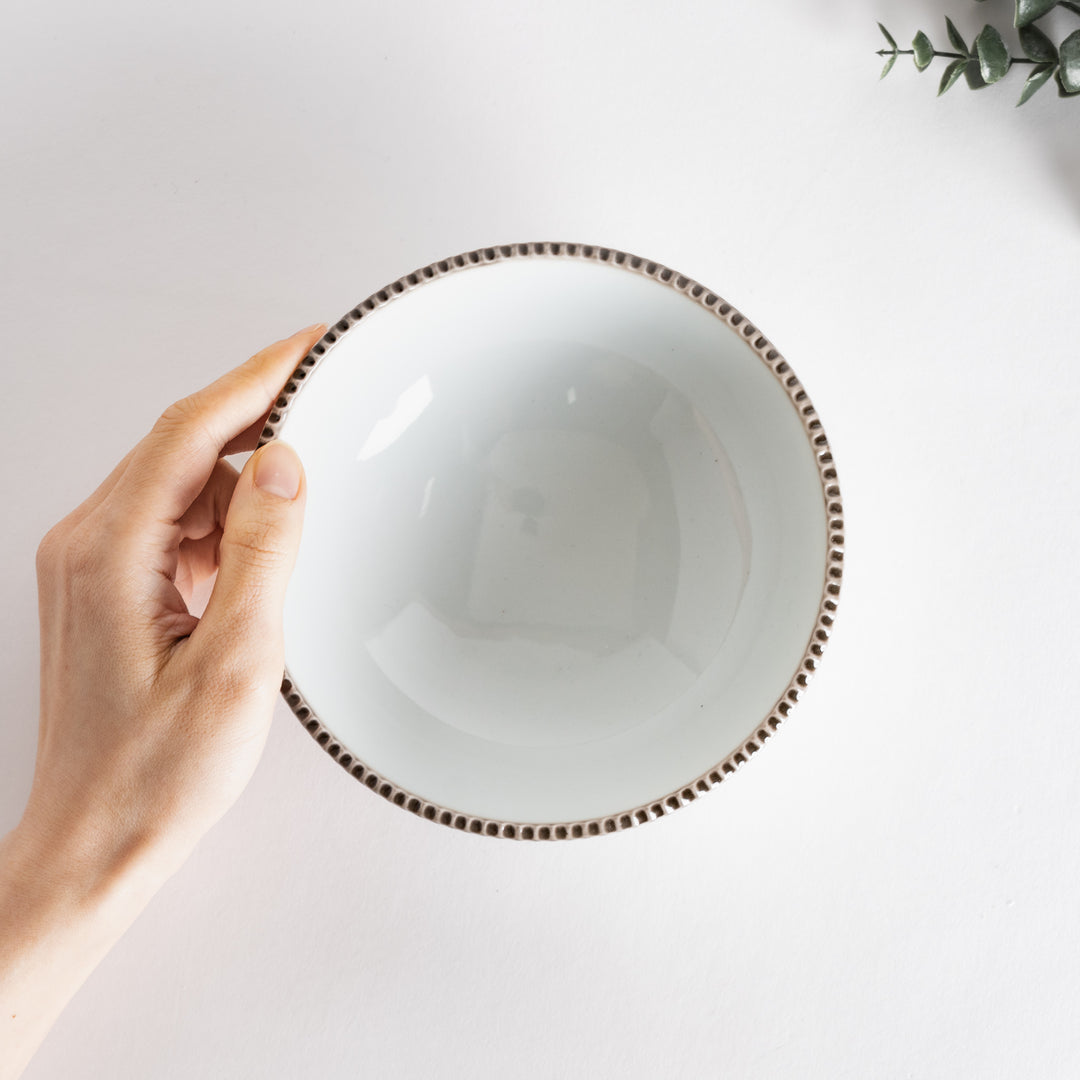 Handheld view of a cereal bowl, showcasing its elegant shape and smooth surface, with a rustic brown scalloped edge.