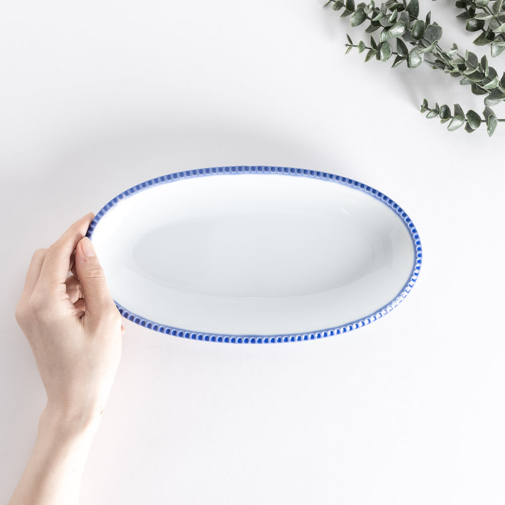 Handheld top-down view of an oval salad plate with a scalloped blue edge.