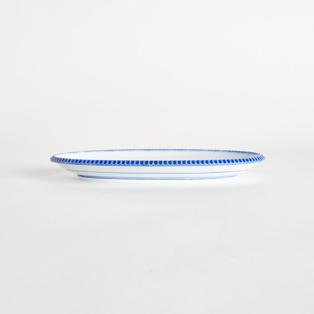 Side view of an oval salad plate showcasing its delicate shape and scalloped blue edge.